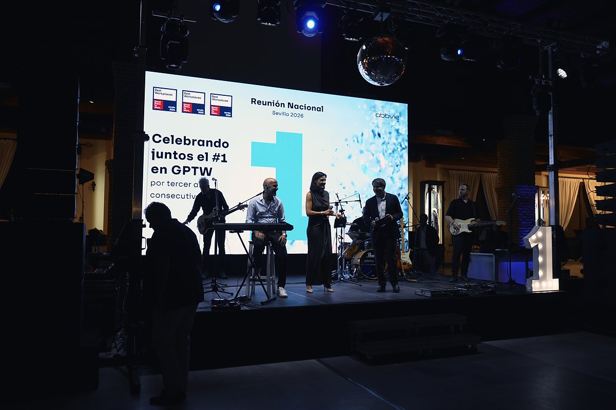 Banda tocando en el escenario de una convención de empresa, con pantalla LED y letras luminosas, de noche