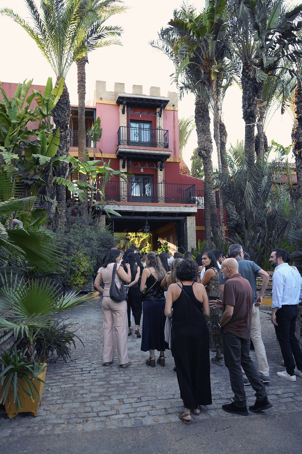 Invitados ante la fachada roja con torreón de una hacienda sevillana, entre palmeras