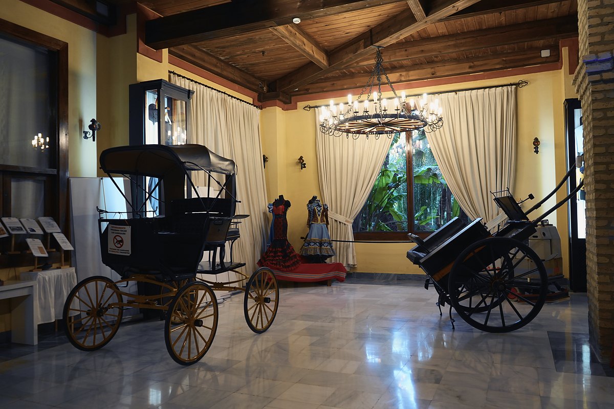 Salón de una hacienda sevillana con artesonado de madera, lámpara de forja y carruajes de época