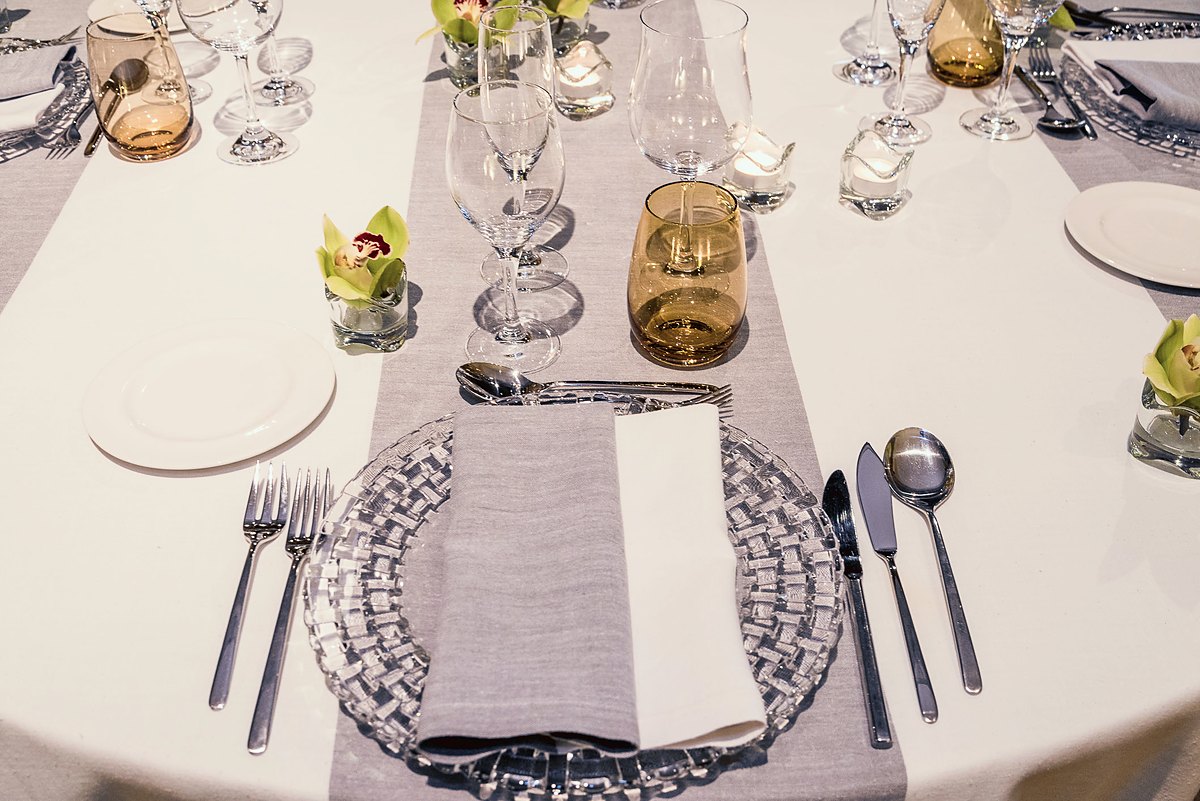 Mesa montada para una comida de trabajo: mantel blanco, camino gris, cristalería y orquídeas en cada cubierto