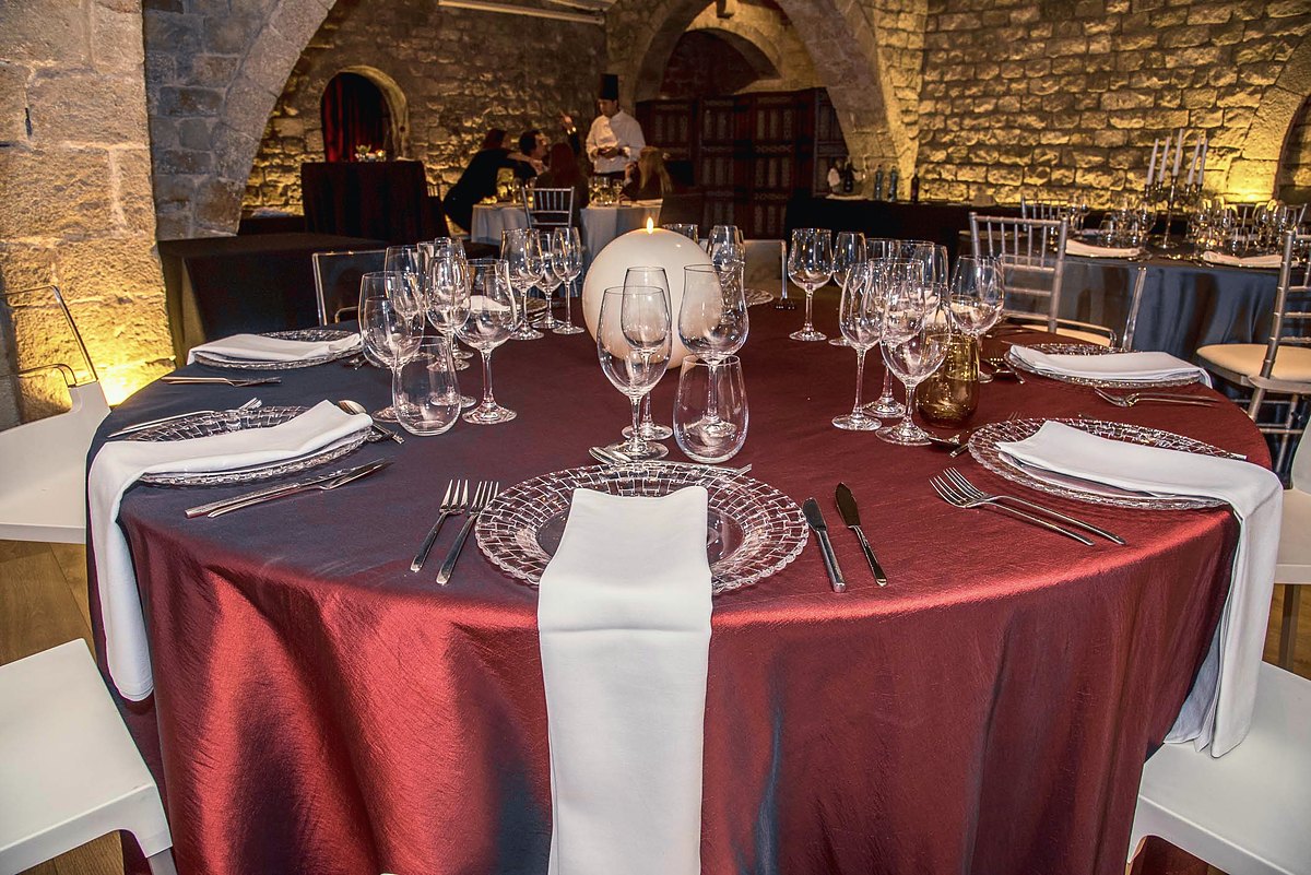 Mesa redonda de gala en una sala abovedada de piedra, lista para la cena