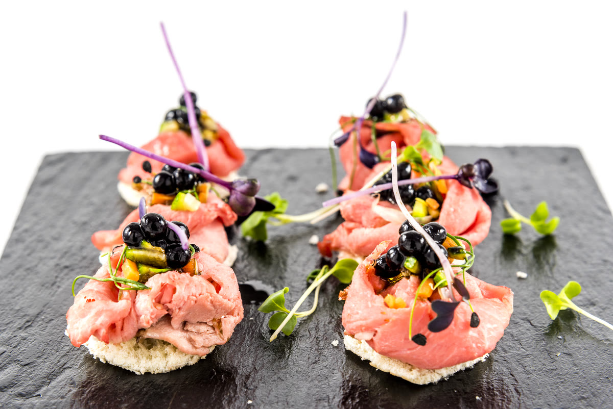Canapés de roast beef con caviar y brotes sobre pizarra, aperitivo de catering para eventos de empresa